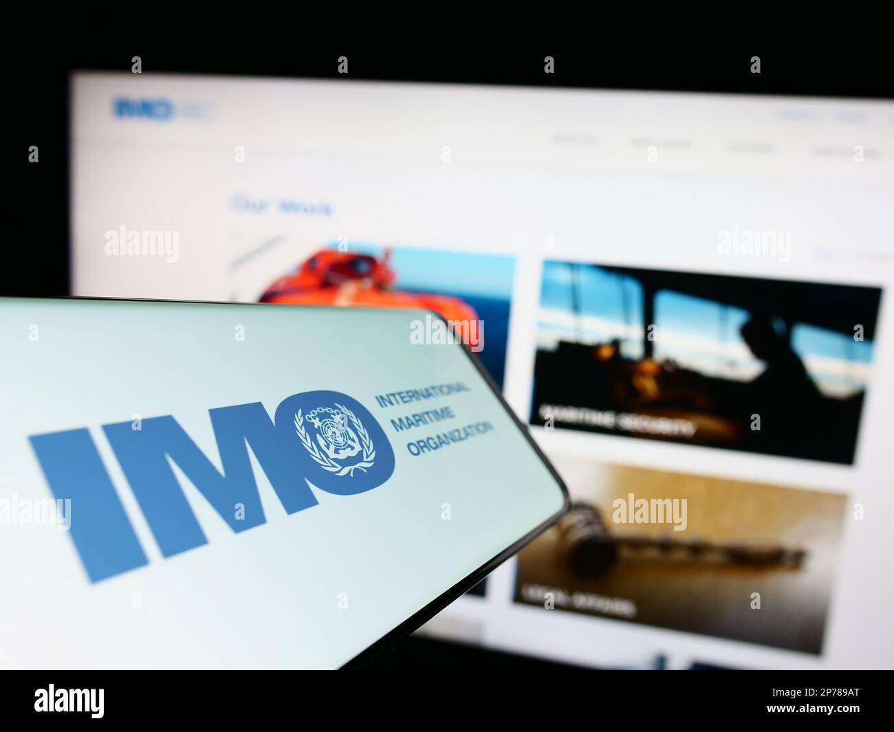 Telefono cellulare con il logo dell'Organizzazione marittima internazionale (IMO) sullo schermo di fronte al sito Web. Messa a fuoco al centro a destra del display del telefono. Foto Stock