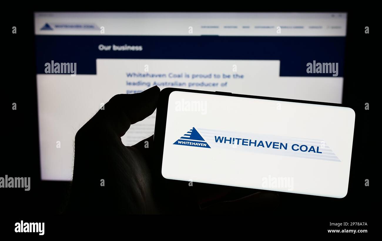 Persona che tiene il cellulare con il logo della società mineraria Whitehaven Coal Limited sullo schermo di fronte al sito web aziendale. Messa a fuoco sul display del telefono. Foto Stock