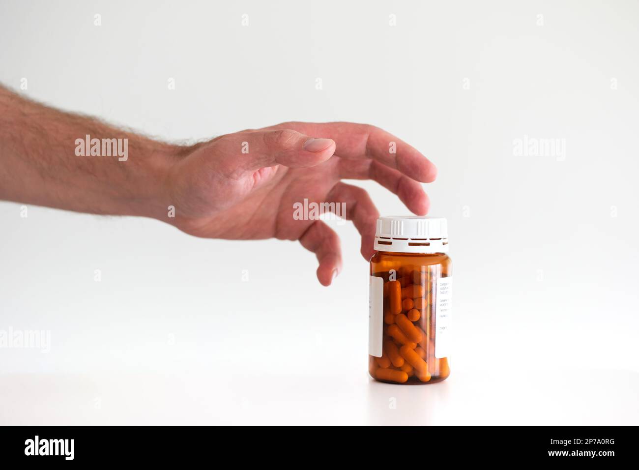 Mano maschio caucasica che raggiunge fuori per afferrare una bottiglia di plastica pillole mediche primo piano shot isolato su bianco. Foto Stock