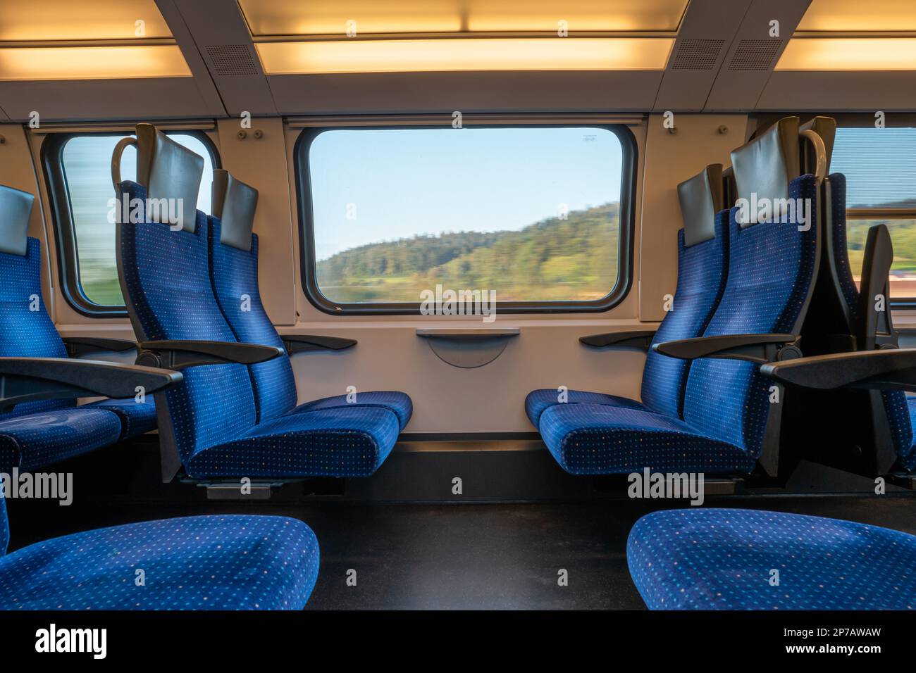 Posti opposti vuoti blu in un treno in movimento. Grande finestra con paesaggio sfocato, di giorno, d'estate, senza persone. Foto Stock