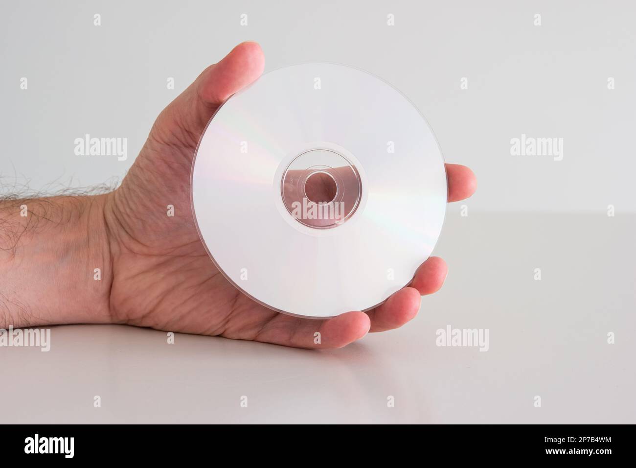 Compact Disc DVD tenuto in mano da uomo caucasico. Vista laterale scrivibile, primo piano ripresa da studio, isolato su bianco. Foto Stock