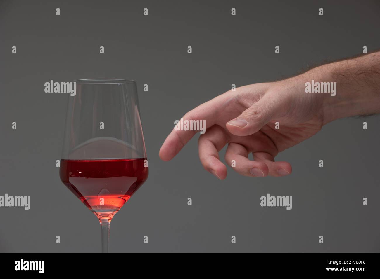 Mano maschio caucasica che arriva fuori per afferrare un bicchiere di vino alto mezzo pieno. Studio, nessuna gente. Foto Stock