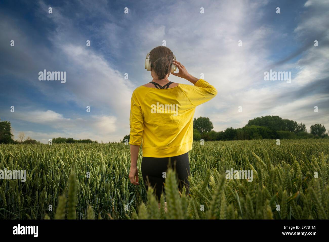 Donna che indossa gli Heaphones in piedi in un campo, allontanandosi da tutto. Foto Stock