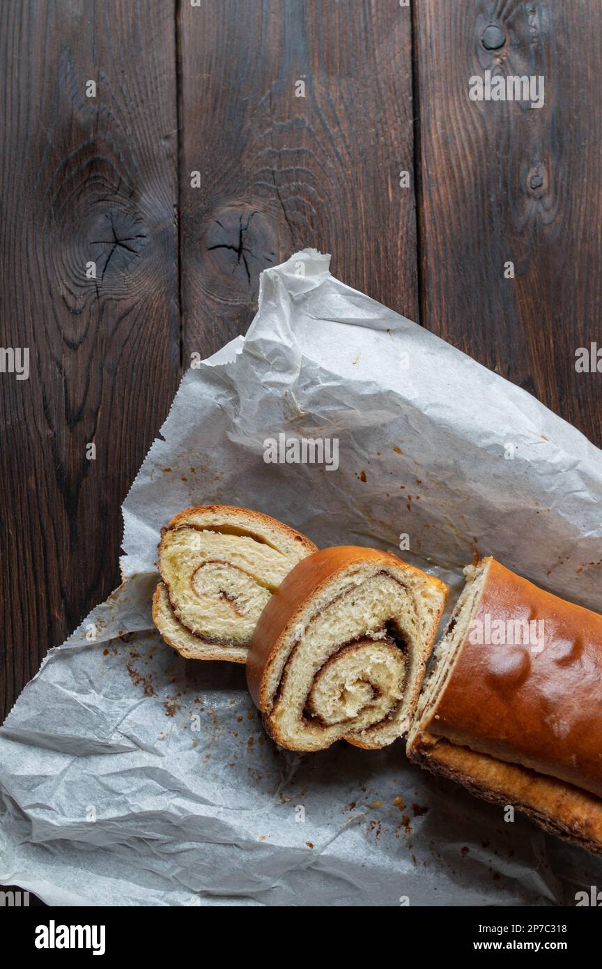 Torta alla cannella cotta in una padella e servita intera e affettata con carta da forno isolata su fondo di tavola di legno scuro. Giacitura piatta con spazio di copia Foto Stock