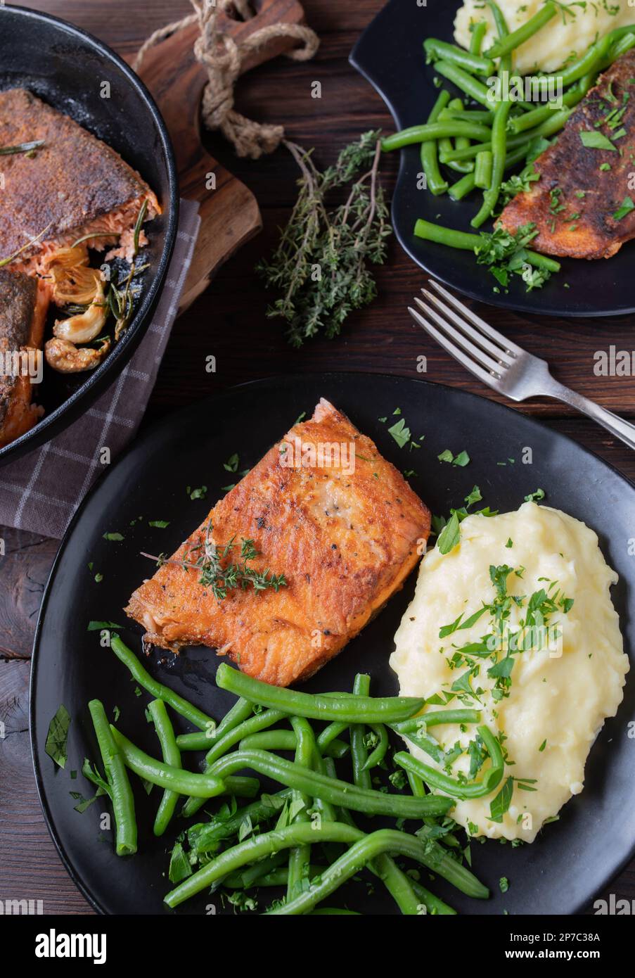 Salmone fritto con pelle. Servito con purè di patate e fagiolini su un piatto scuro su un tavolo rustico e di legno. Vista dall'alto Foto Stock