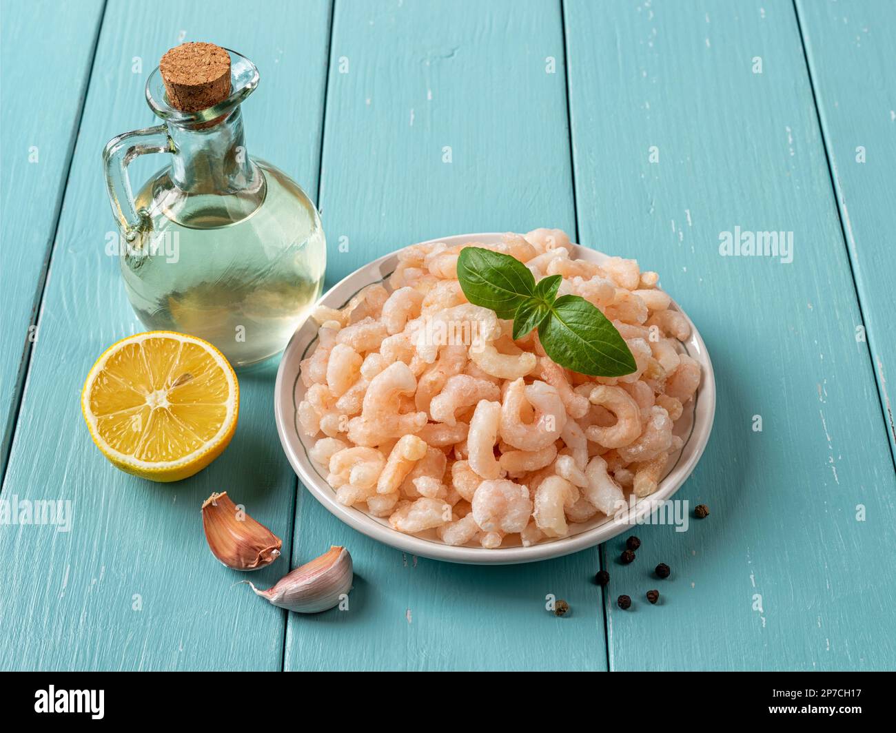 Piatto di gamberetti bolliti surgelati su tavolo di legno blu. Code di gamberi sbucciate cotte, limone, aglio e olio d'oliva preparati per la cottura. Vista dall'alto. Foto Stock
