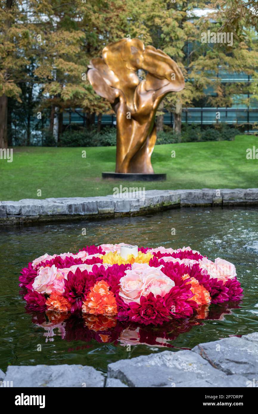 Fiori di rangoli colorati galleggiano in una piscina d'acqua di fronte all'opera d'arte in bronzo intitolata Fortuna di Helaine Blumenfeld nel Jubilee Park, Canary Wharf Foto Stock