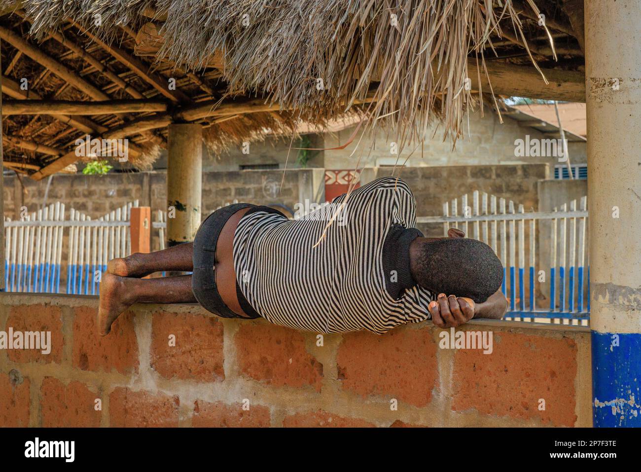foto di un uomo precariosamente equilibrato veloce addormentato longitudinalmente su una stretta parete di mattoni vista posteriore in luce del giorno Foto Stock