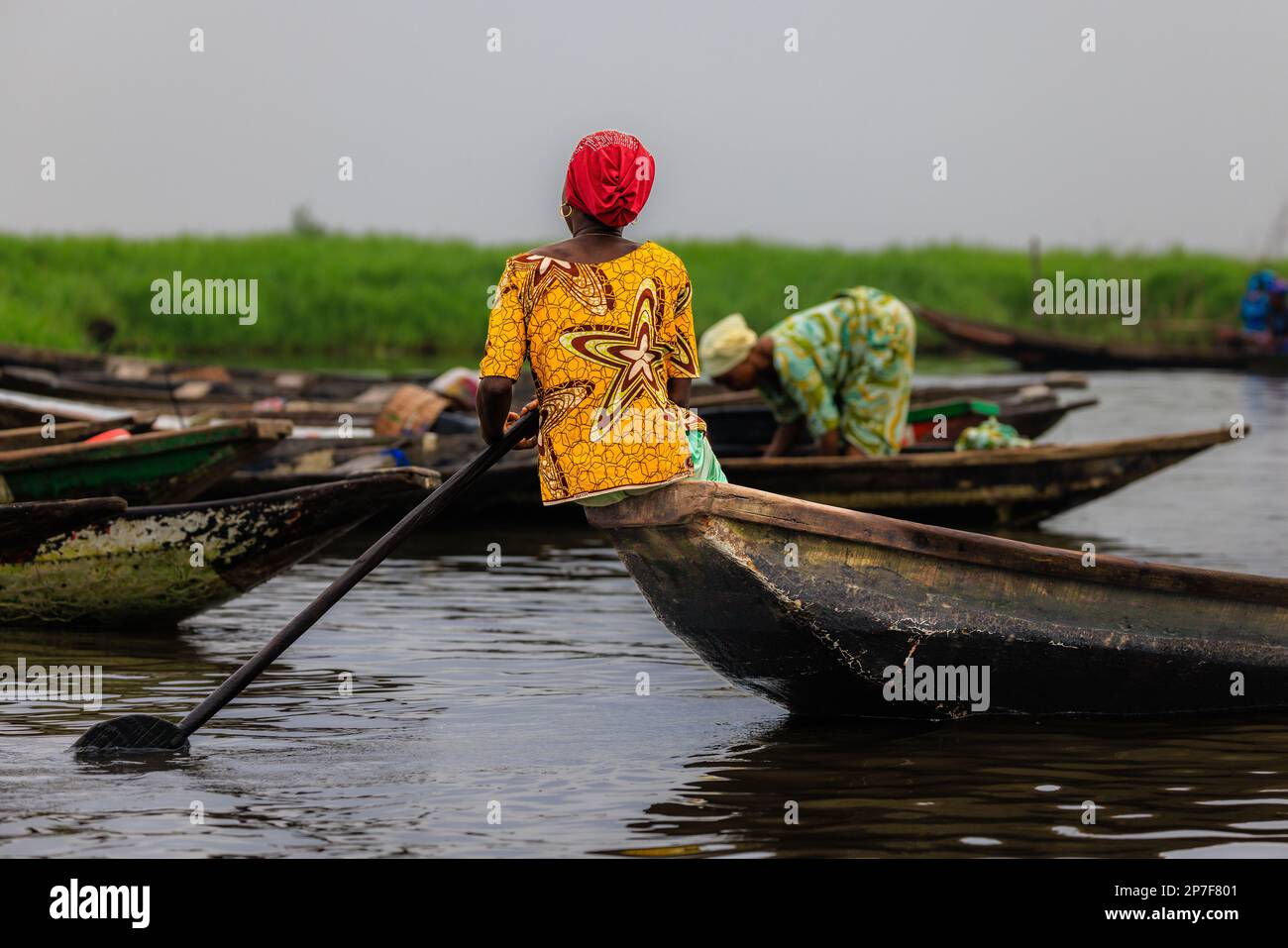 La signora africana arroccò sulle pagaie di poppa per manovrare la sua barca di legno al mercato galleggiante a Ganvie sul lago nokwie in Benin Foto Stock