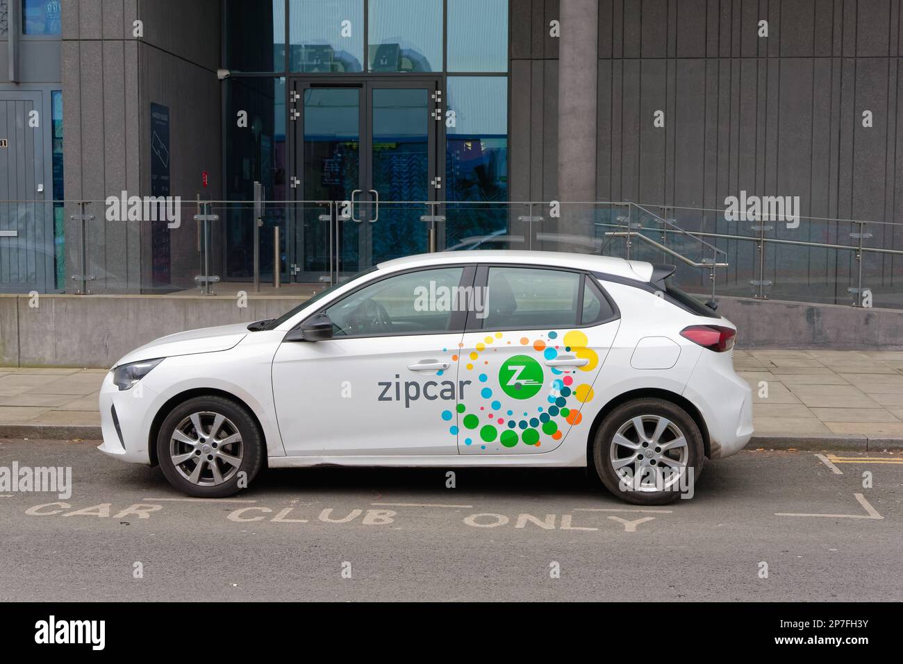 Una berlina bianca Zipcar parcheggiata in una marcata 'Car Club Bay' fuori da un moderno edificio nel centro di Londra, Inghilterra UK Foto Stock