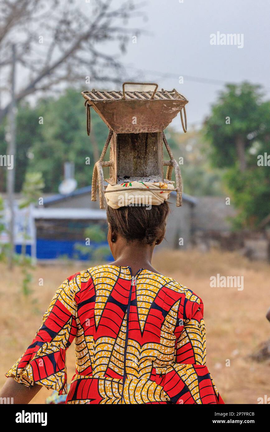 wow che è un barbecue portatile con griglia in mat cast e bilanciato sulla testa di una donna africana vestita in modo colorato Foto Stock