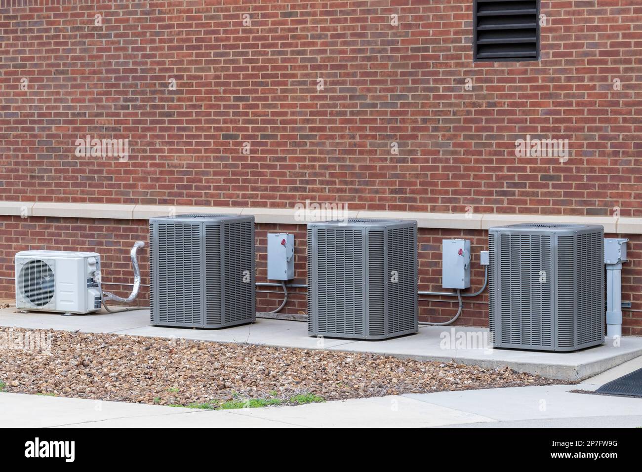 Immagine orizzontale di quattro compressori dell'aria condizionata all'esterno di un edificio scolastico. Foto Stock