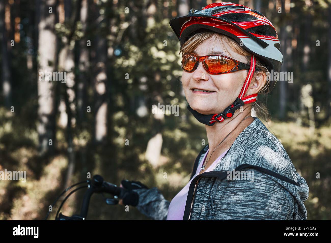 Donna attiva in bicicletta su strada forestale. Donna in bicicletta in fuoristrada percorso durante il giorno delle vacanze estive. Donna che indossa casco e guanti da bicicletta Foto Stock