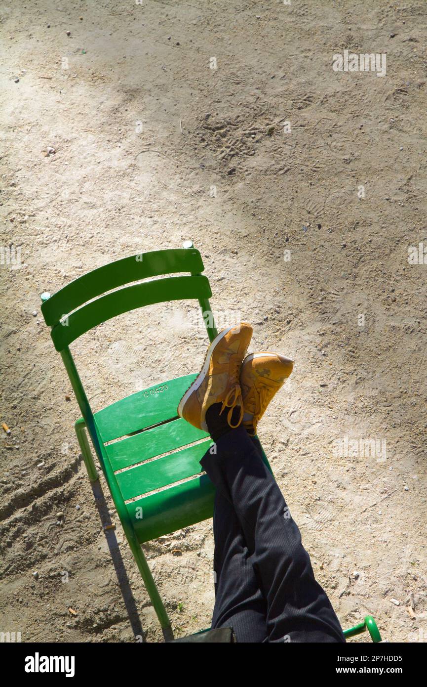 Vista guardando giù sulle gambe di Una persona con i piedi su una sedia rilassante nella primavera Sunshine, Jardin Tuileries Parigi Francia Foto Stock