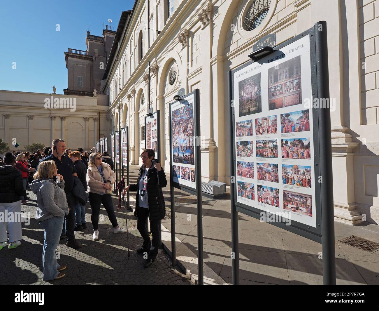 Poiché non è consentito parlare nella Cappella Sistina, le guide turistiche utilizzano una delle numerose serie di 3 poster nel cortile, prima di entrare. Foto Stock