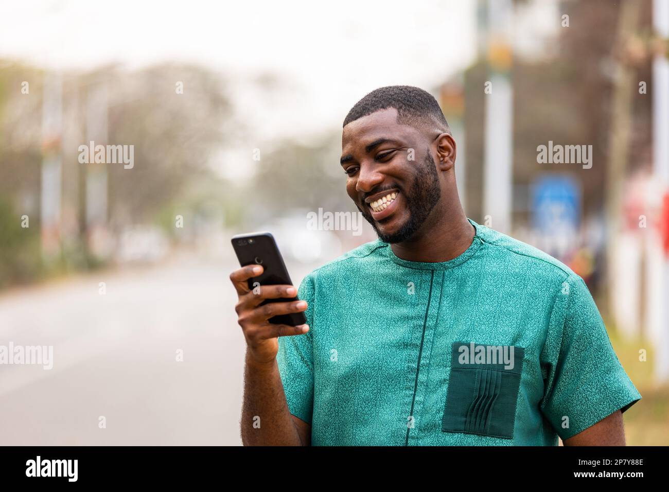 African Young Man che utilizza un dispositivo mobile per i social media, Ritratto di un maschio nero che tiene uno smartphone Foto Stock