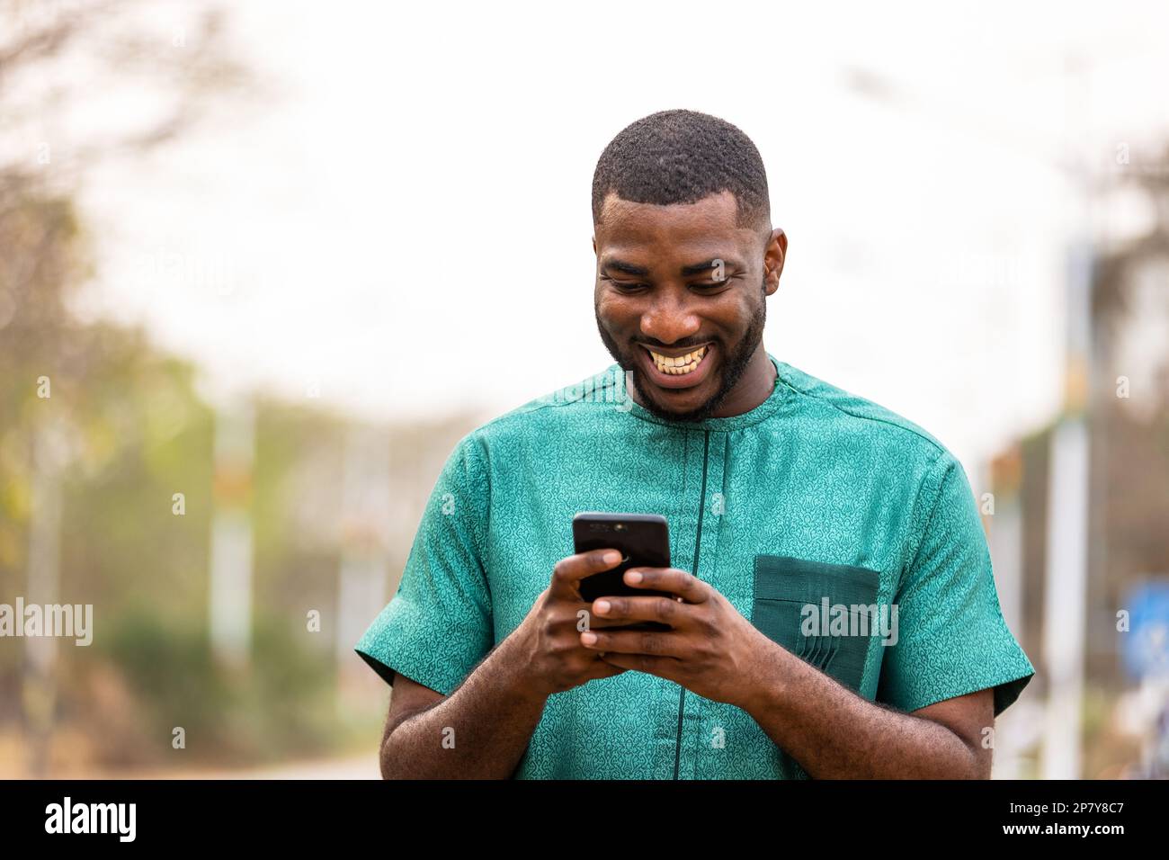 Giovane uomo africano Mobile banking in movimento con smartphone, Ritratto di un uomo ghanaiano in possesso di cellulare Foto Stock