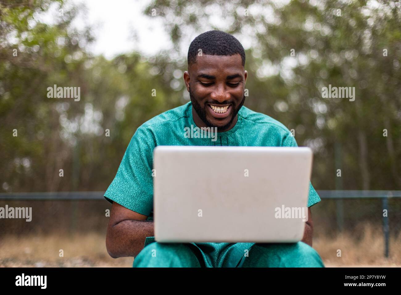 Giovane uomo africano con computer portatile all'aperto, che richiede l'ingresso all'università online. Foto Stock
