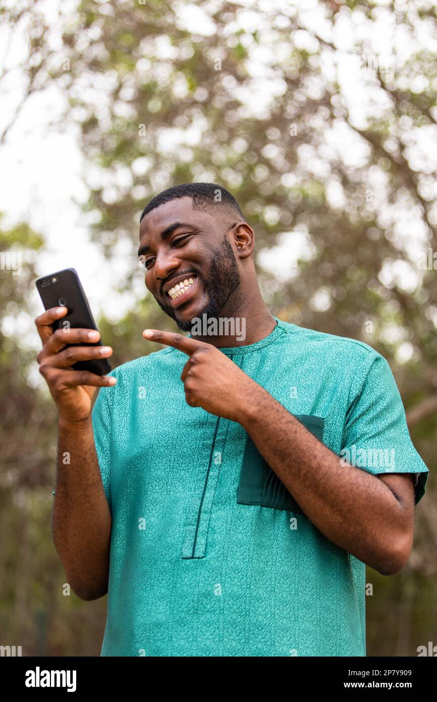 Felice giovane uomo africano che SMS e sorridendo, utilizza il suo telefono cellulare per lo shopping online. Foto Stock