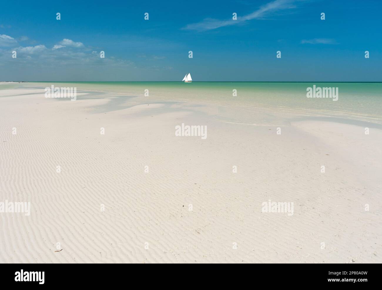 Spiaggia di sabbia bianca su un'isola tropicale con nave a vela all'orizzonte contro il cielo blu Foto Stock