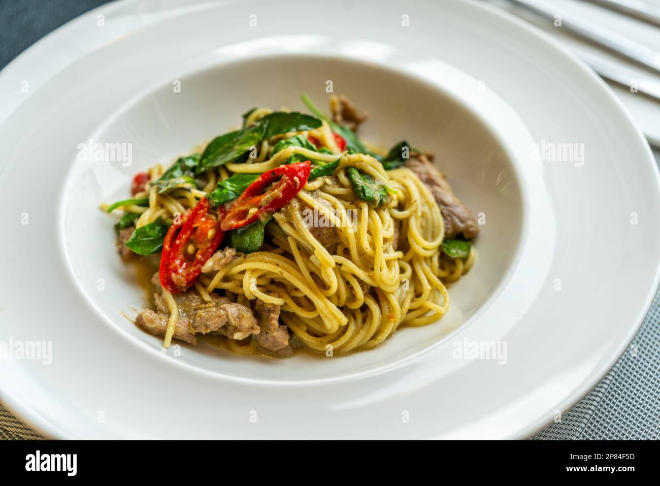 Delizioso cibo di fusione tailandese, spaghetti fritti mescolati con curry verde tailandese e carne. Bella cucina tailandese in moderno piatto bianco su un tavolo nel ristorante, Foto Stock