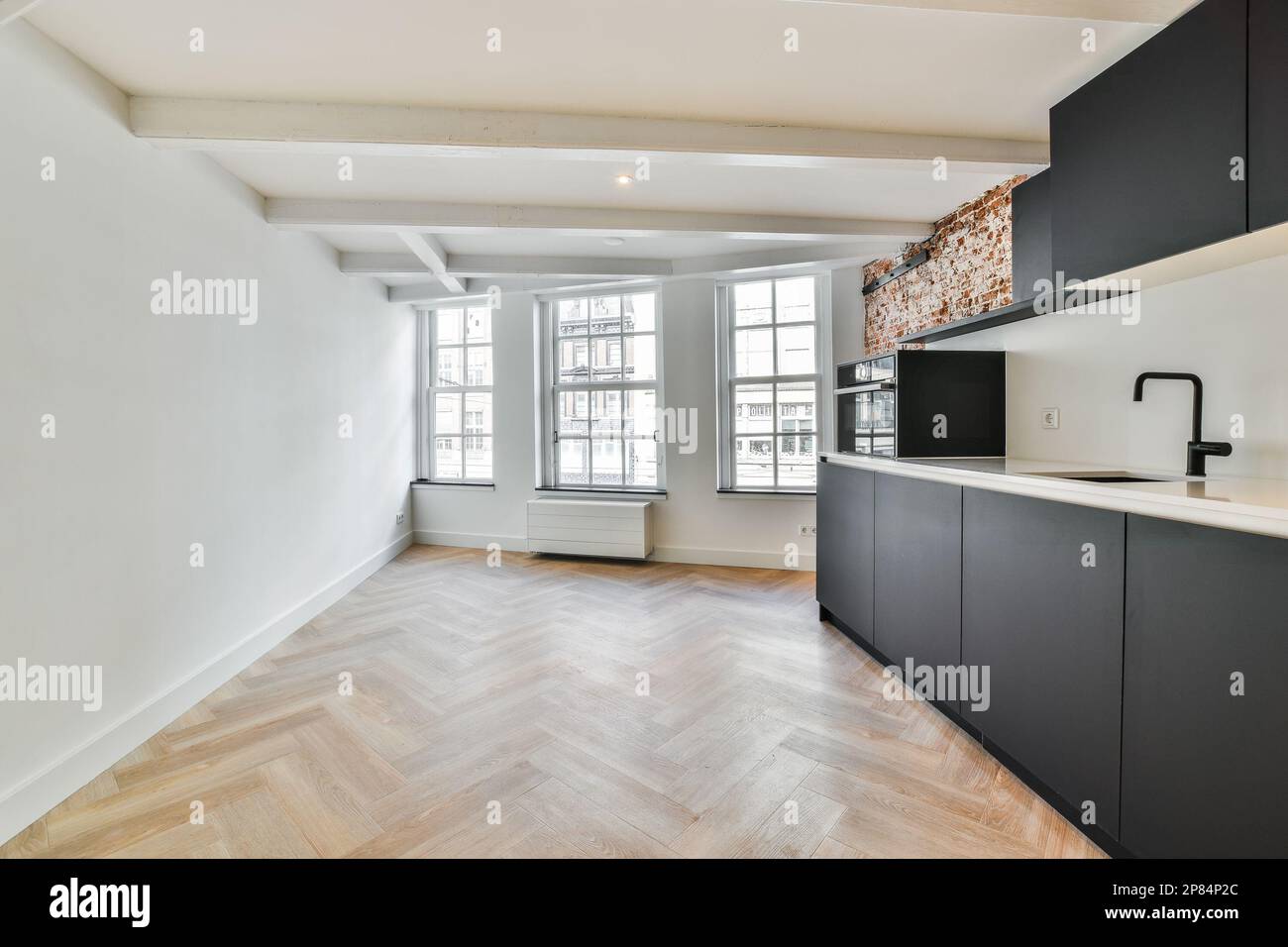 una cucina vuota con pavimento in legno e pareti bianche in una stanza che ha pavimenti in legno duro, armadi neri e grandi finestre Foto Stock