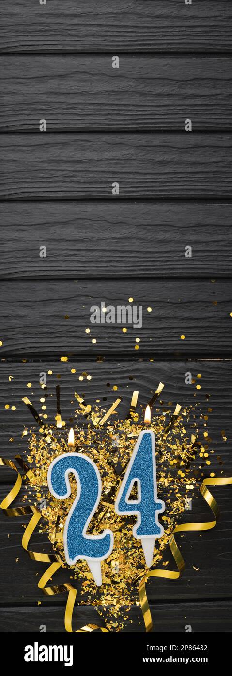 Numero 24 candela blu da celebrazione e coriandoli d'oro su fondo di legno scuro. 24th biglietto di compleanno. Concetto di anniversario e compleanno. Banner verticale. Foto Stock