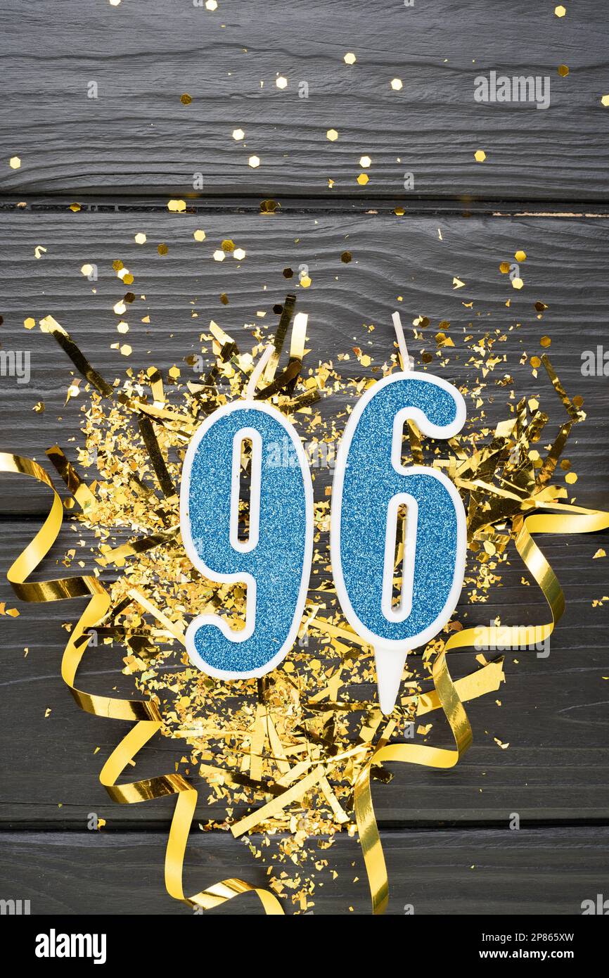 Numero 96 candela blu da celebrazione e coriandoli d'oro su fondo di legno scuro. 96th biglietto di compleanno. Concetto di anniversario e compleanno. Banner verticale. Foto Stock