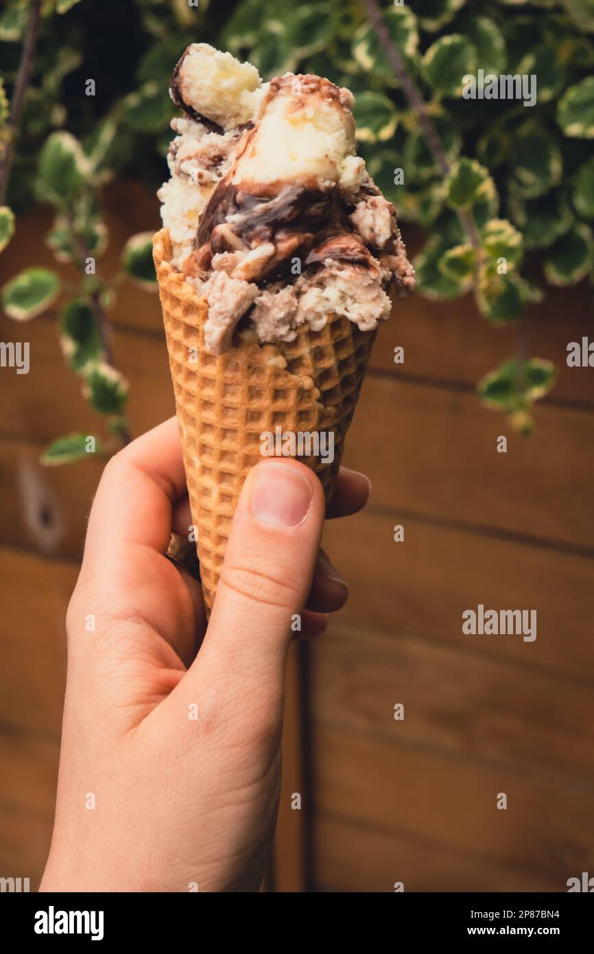 Donna che tiene un delizioso gelato alla vaniglia americana al cioccolato. Gustoso gelato fatto in casa nel cono dei waffle. Gelato vegano senza glutine senza latticini. Foto Stock