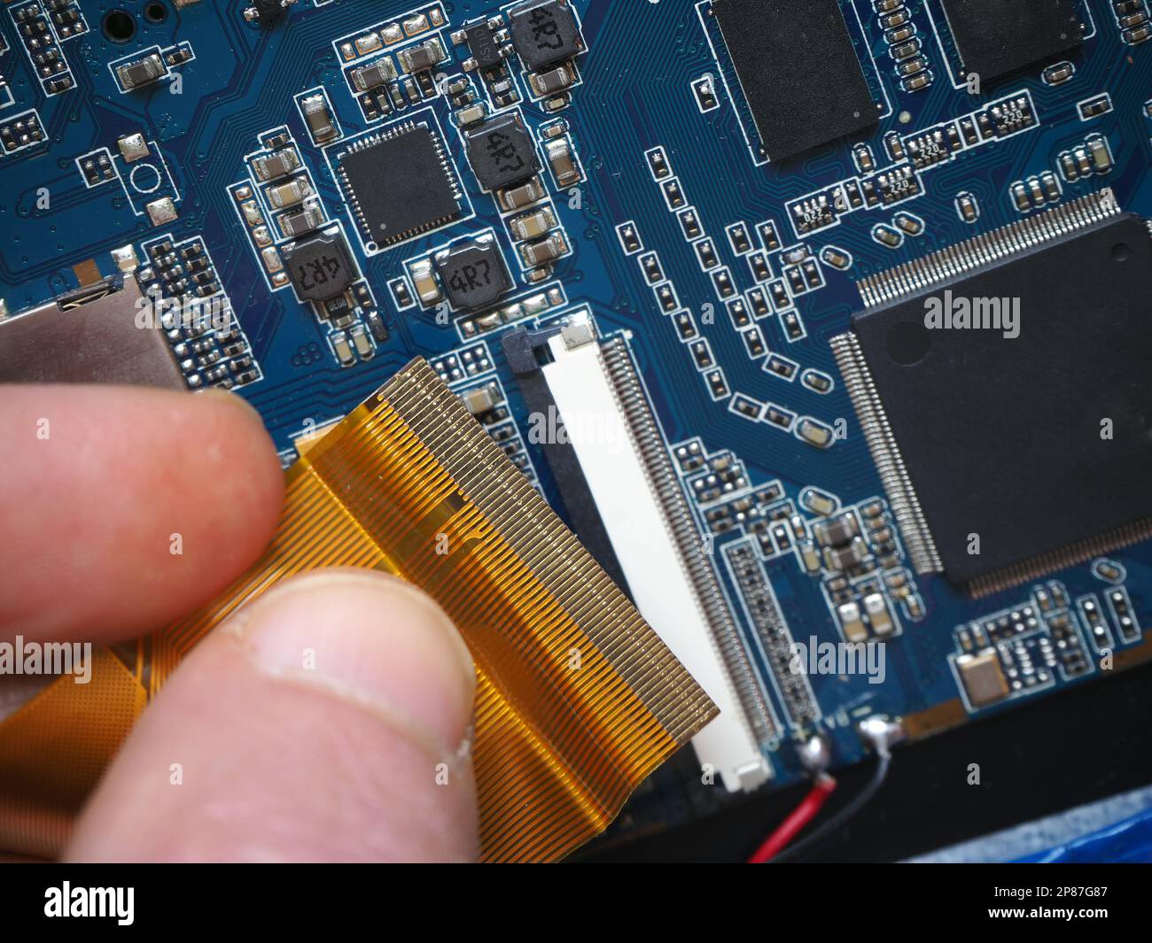 Il tecnico installa il cavo piatto flessibile nel connettore sulla scheda. Scheda elettronica con processore. Industria dei semiconduttori. Foto Stock