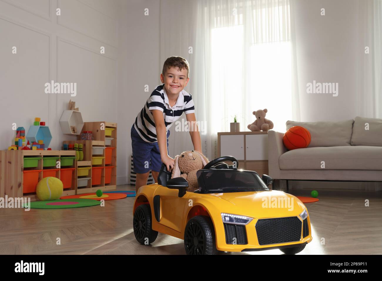 Un ragazzino carino che gioca con un'auto giocattolo e un coniglietto imbottito a casa Foto Stock