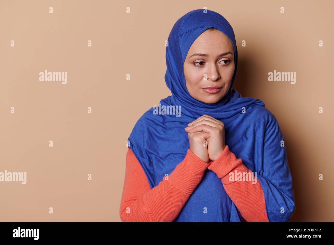 Donna musulmana di mezza età in hijab blu e look speranzoso, con le mani piegate a livello del petto, prega Allah per la pace. Islam Foto Stock