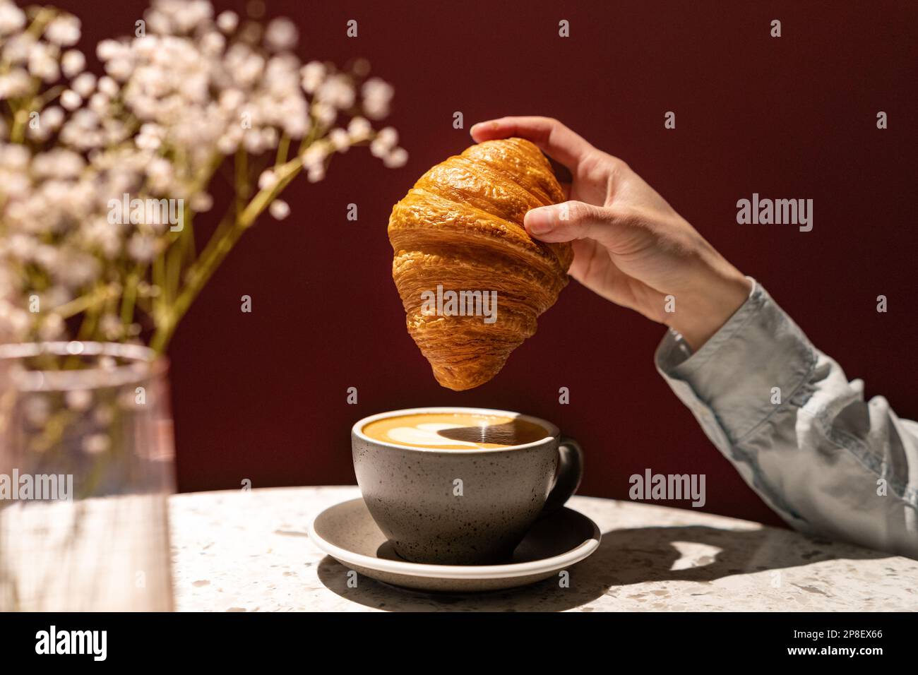 Primo piano di una donna che tuffa un croissant in una tazza di caffè Foto Stock