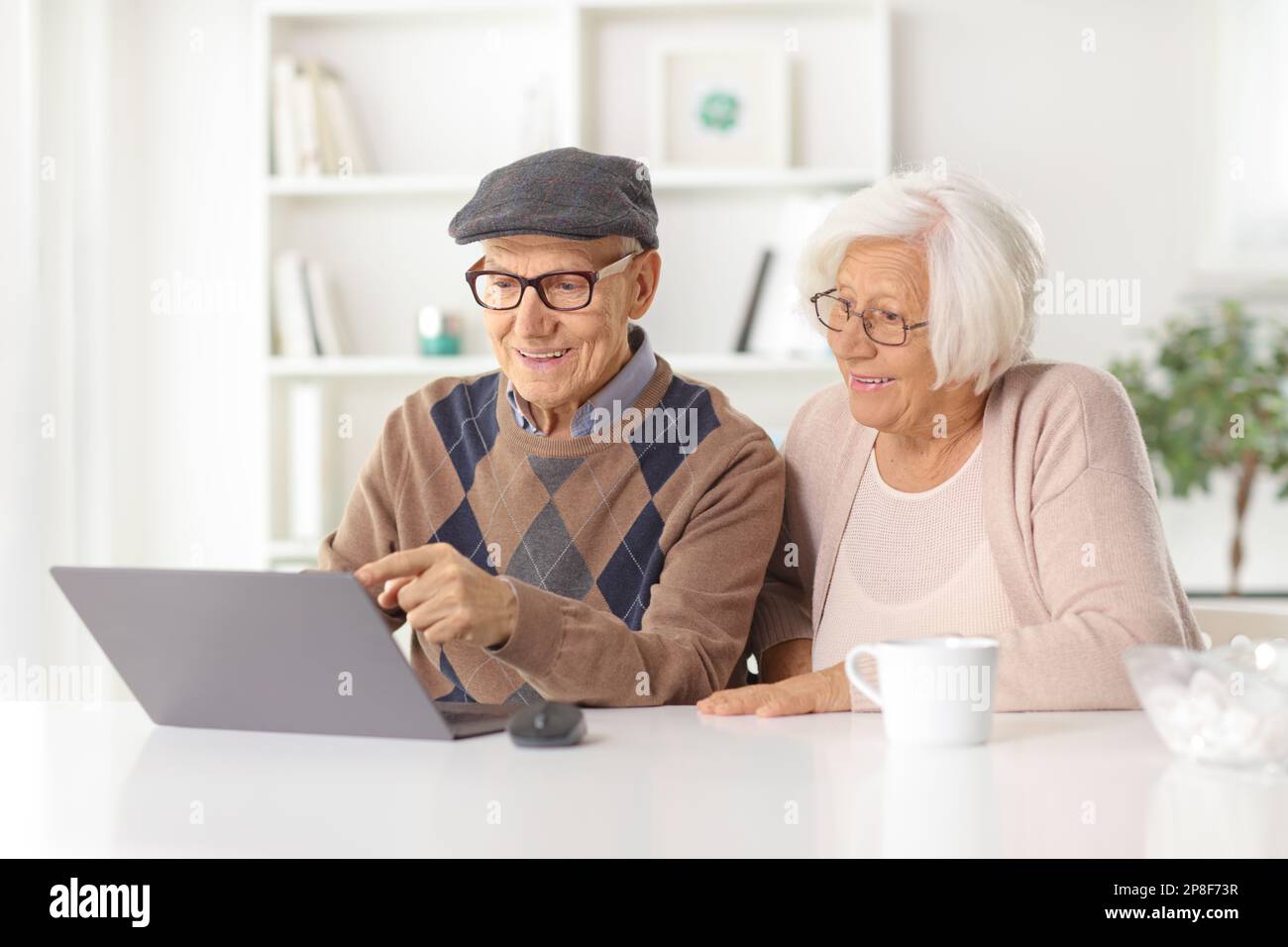 Felice coppia anziana seduta a casa di fronte al computer portatile Foto Stock