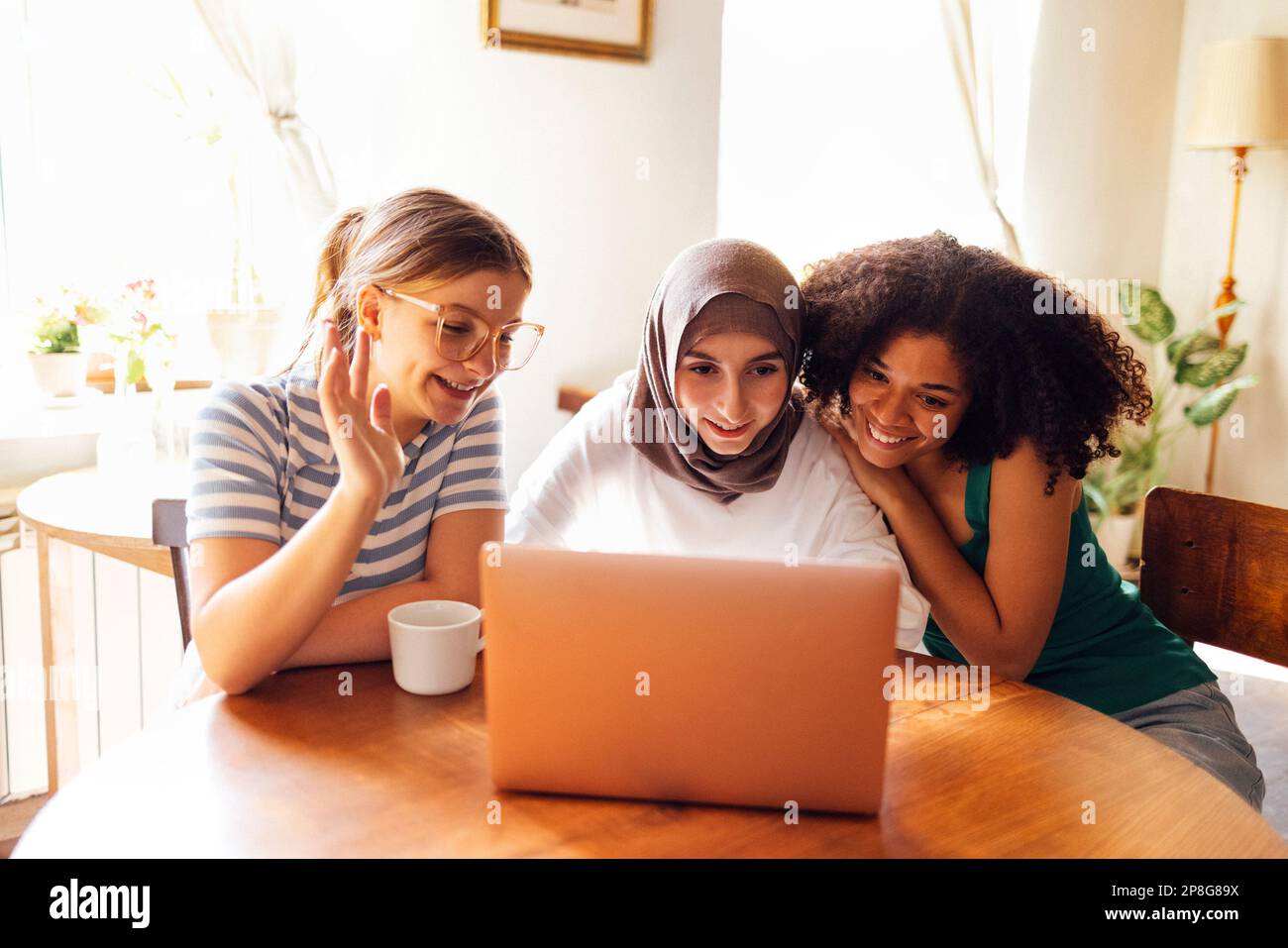 Tre graziose adolescenti di diverse nazionalità guardano lo schermo del notebook e ridono. Gli adolescenti caucasici, afro americani e musulmani sono Foto Stock