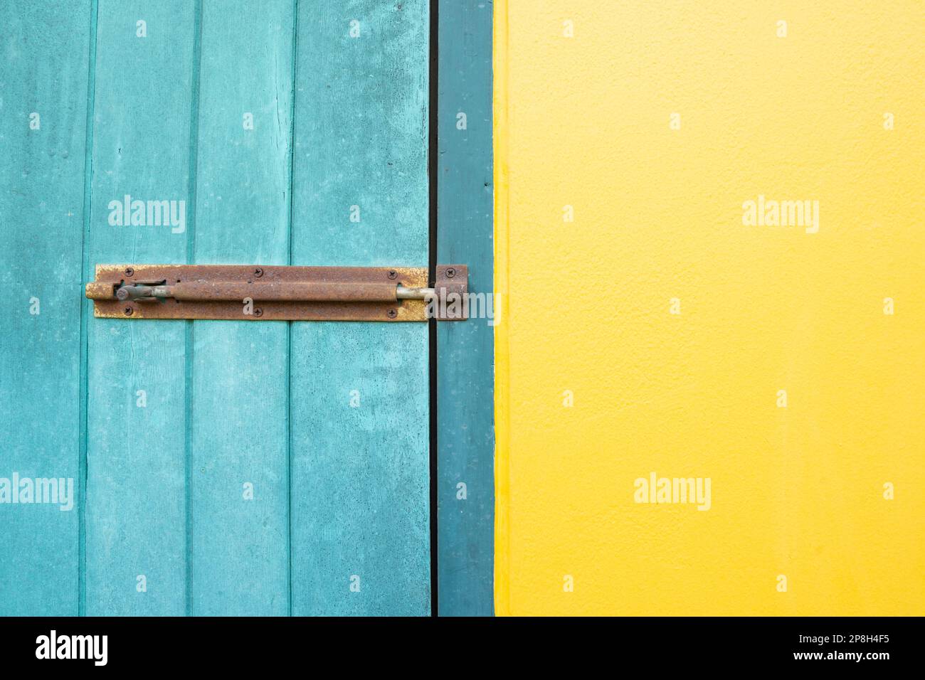 Il lucchetto chiuso è appeso alle porte a muro gialle e blu. Foto Stock