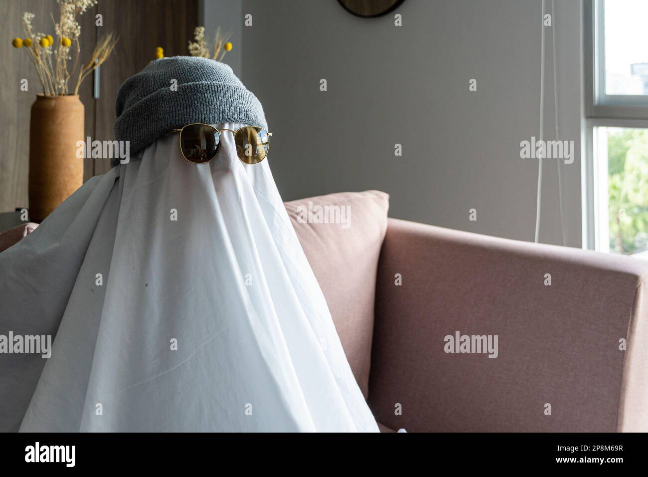 Una persona che indossa un cappello e occhiali da sole neri su un panno bianco che assomiglia a un fantasma Foto Stock