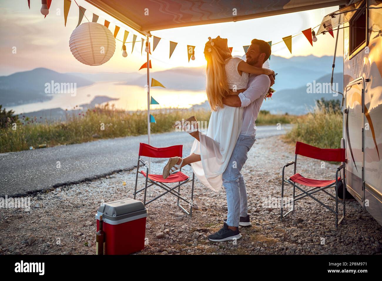 uomo caucasico che tiene in braccio bella bionda con i piedi del terreno, all'aperto in natura di fronte a un camper Foto Stock