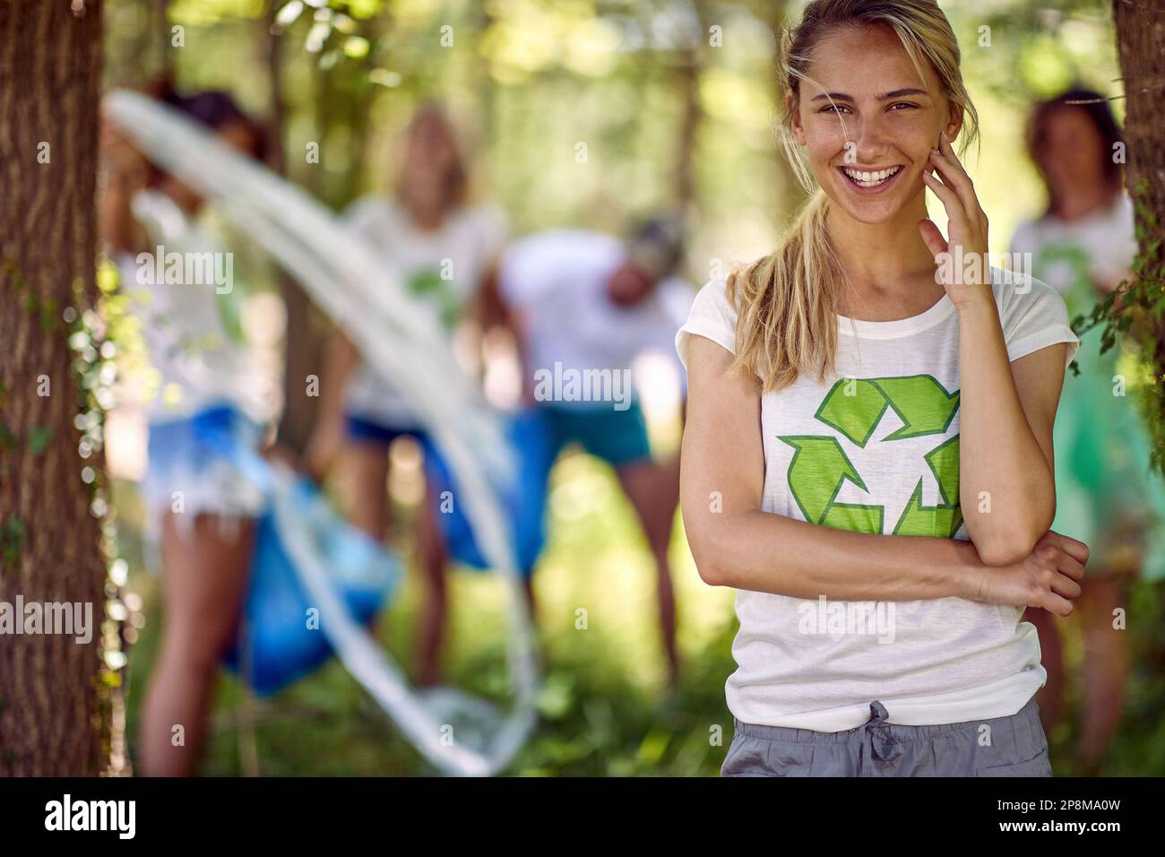 Giovane e gioiosa donna volontaria. Gruppo di persone che raccolgono rifiuti in natura. Ambientalismo, verde, concetto di stile di vita. Foto Stock