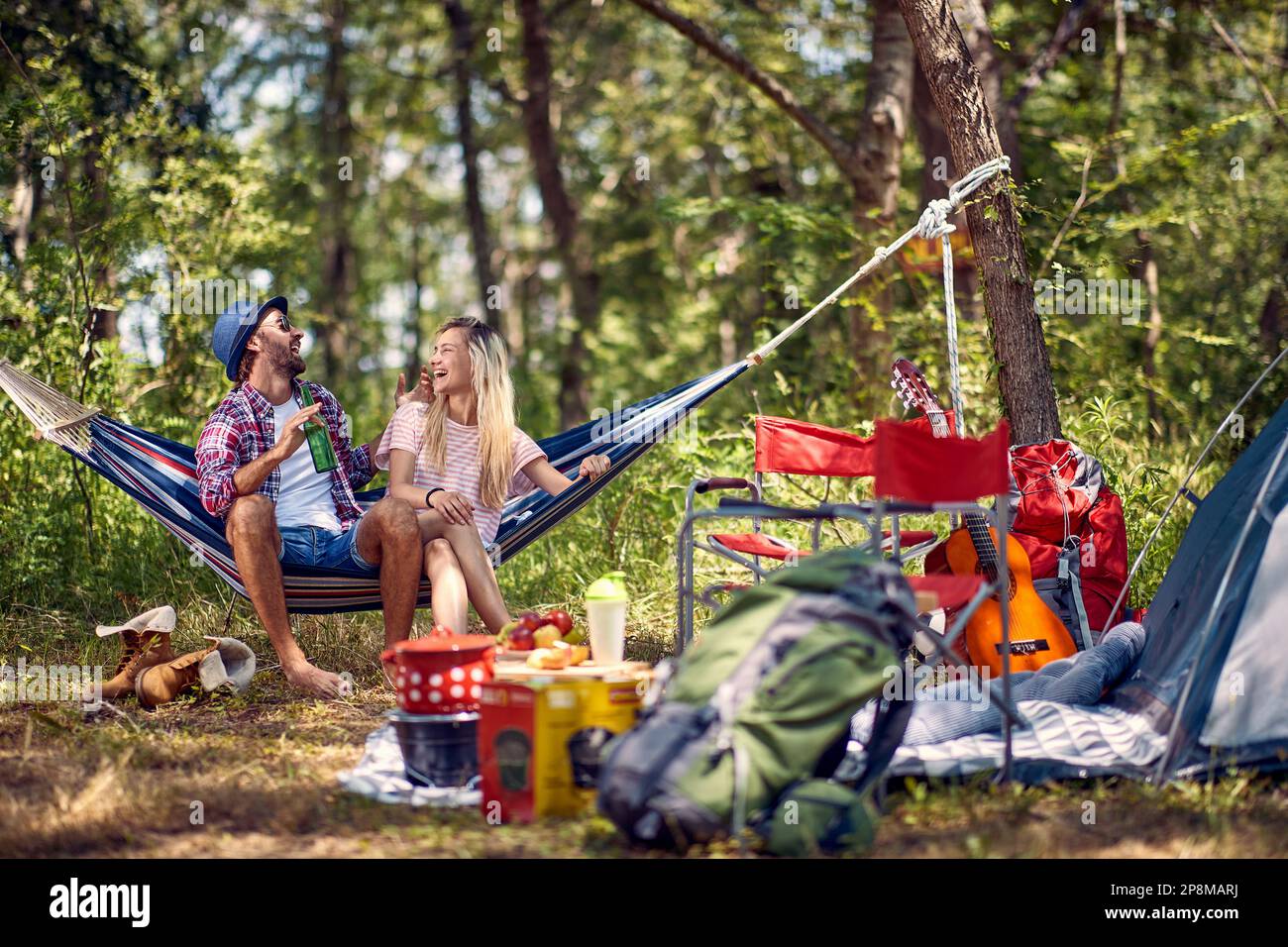 Giovane coppia allegra hipster che ha piccolo parlare e sedersi in amaca, godendo il campeggio nella natura. Vacanza, tempo libero, divertimento, concetto di stile di vita. Foto Stock