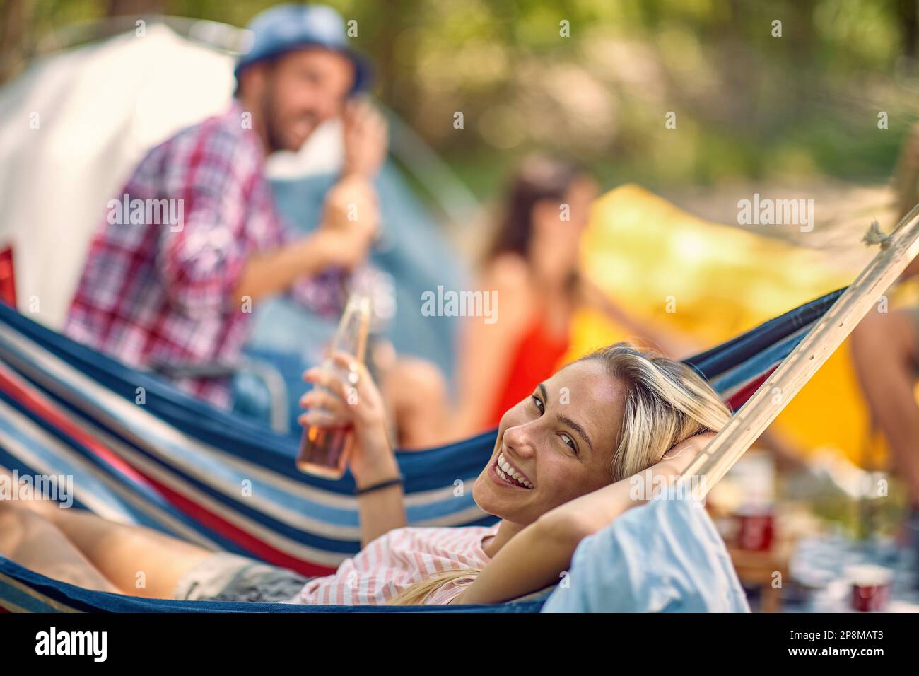 Amici che hanno picnic nella natura, all'aperto. Giovane donna che si posa in amaca tenendo birra. Vacanza, convivenza, divertimento, concetto di stile di vita. Foto Stock