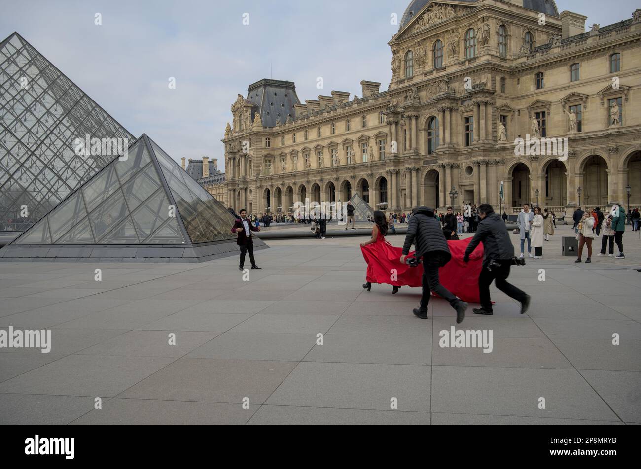 Donna in vestito rosso che corre con un equipaggio di macchina fotografica verso il suo compagno al Louvre durante l'inverno. Parigi, Francia Foto Stock