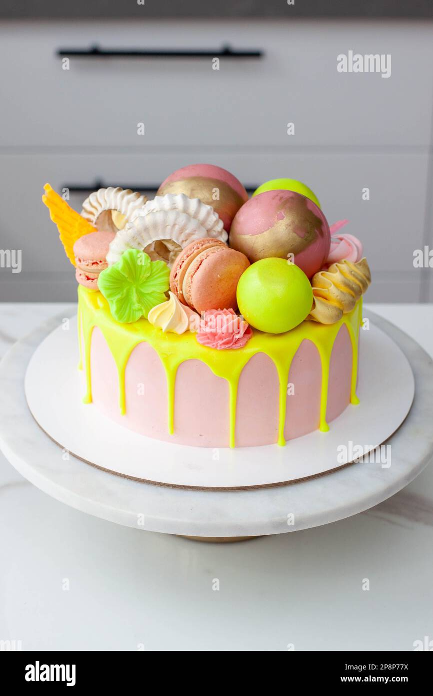 Verde neon, lime e rosa flebo torta di compleanno felice sormontata con fiori assortiti di cioccolato color arcobaleno, palle, meringhe e caramelle Foto Stock