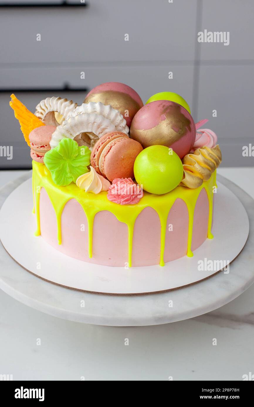 Verde neon, lime e rosa flebo torta di compleanno felice sormontata con fiori assortiti di cioccolato color arcobaleno, palle, meringhe e caramelle Foto Stock