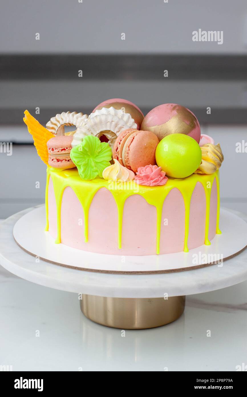 Verde neon, lime e rosa flebo torta di compleanno felice sormontata con fiori assortiti di cioccolato color arcobaleno, palle, meringhe e caramelle Foto Stock