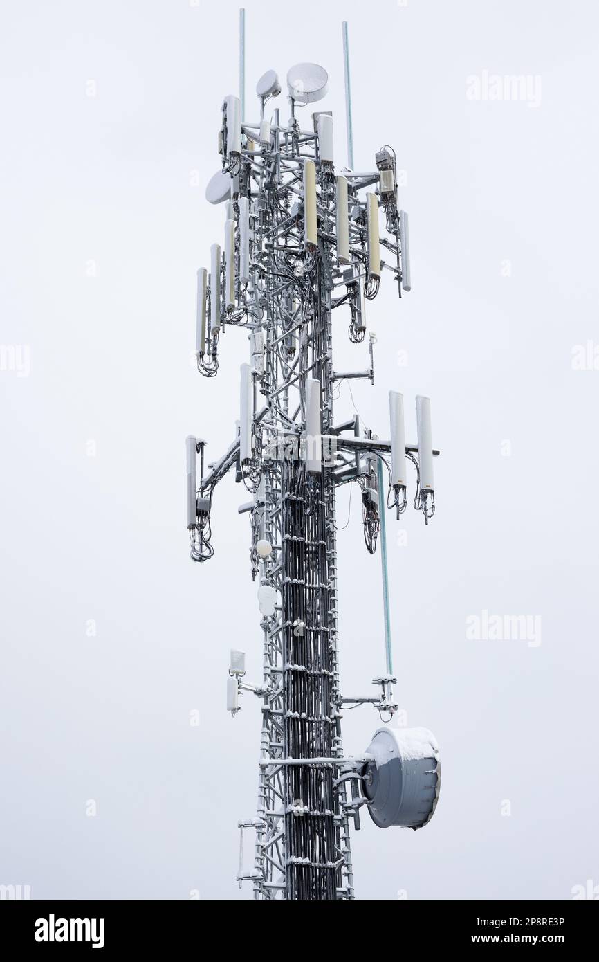 Una torre cellulare innevata contro un cielo bianco. Foto Stock