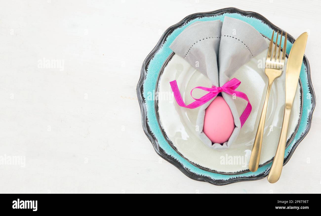 Decorazione e impostazione del tavolo di Pasqua, uovo di Pasqua in tovagliolo grigio, posate dorate su piatti, sfondo bianco Foto Stock