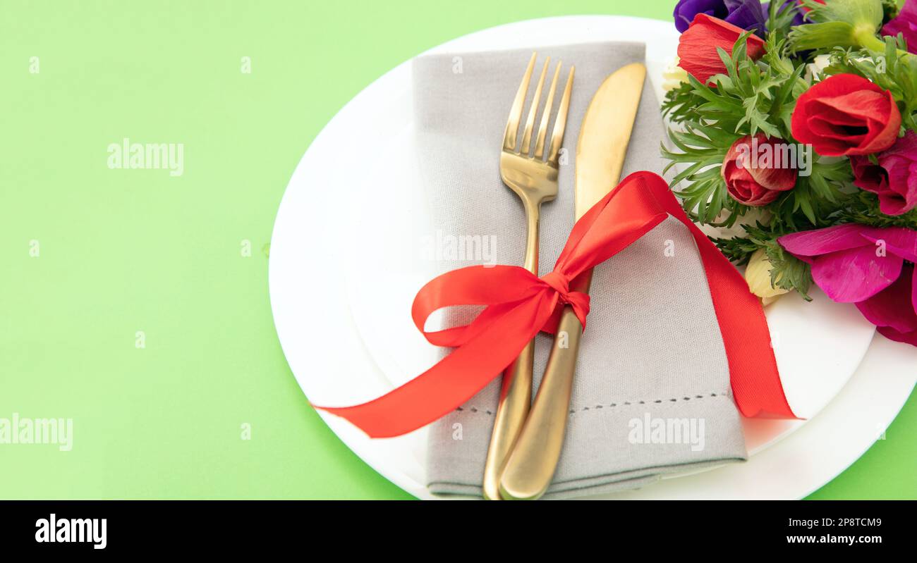 Tavolo da primavera, decorazione fiori selvatici, tovagliolo e posate dorate su piatti bianchi, sfondo verde pastello, vista ravvicinata Foto Stock