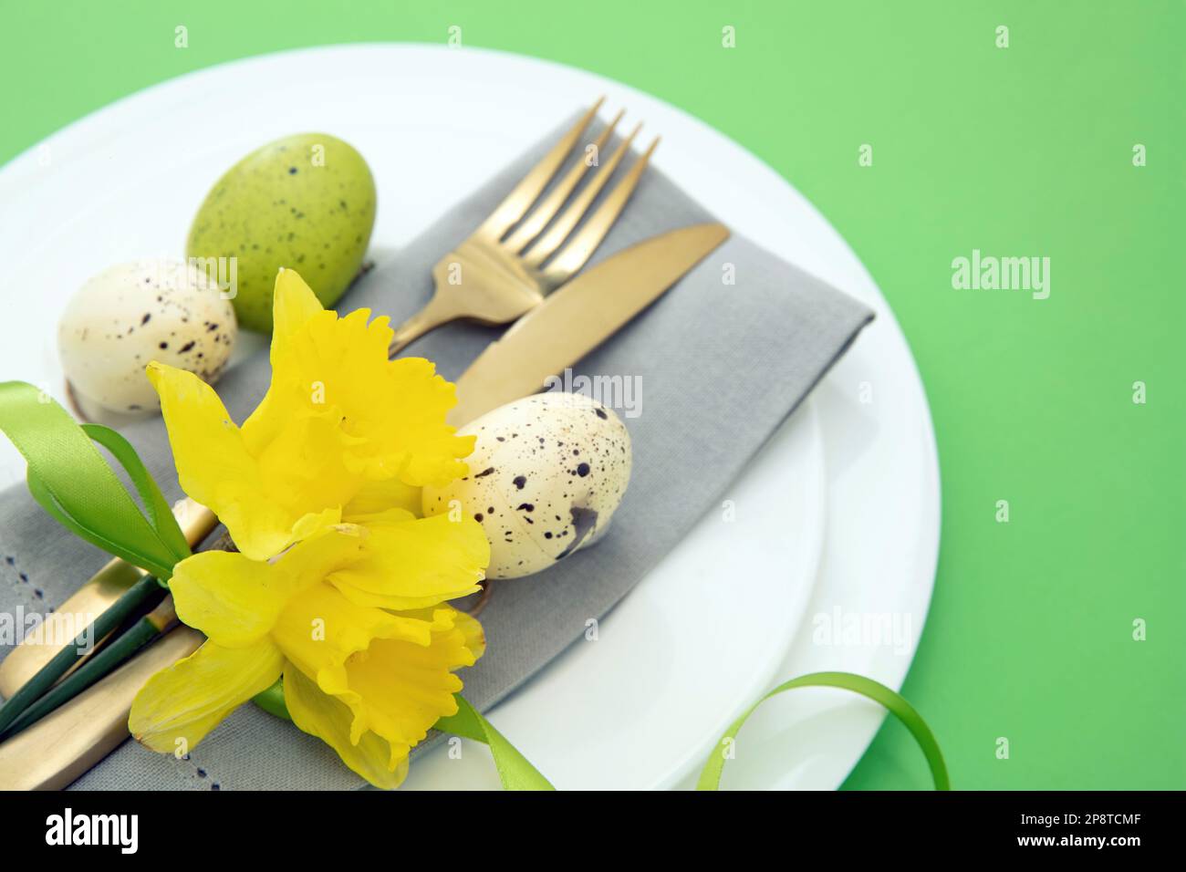 Tavola di Pasqua, fiori primaverili e uova decorazione, tovagliolo e posate dorate su piatti bianchi, sfondo verde pastello Foto Stock