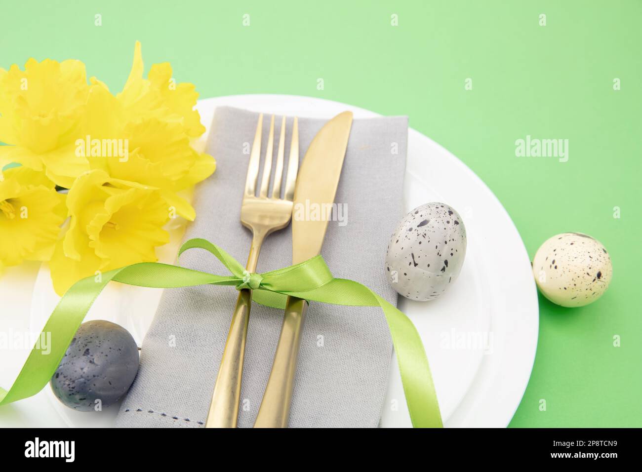 Tavola di Pasqua, fiori primaverili e uova decorazione, tovagliolo e posate dorate su piatti bianchi, sfondo verde pastello Foto Stock
